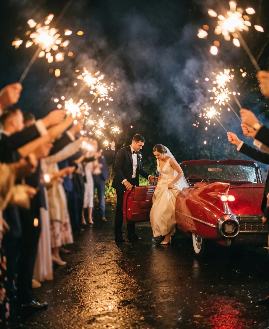 Bride and groom stepping into a red 1960 Cadillac convertible during a sparkler send off at night